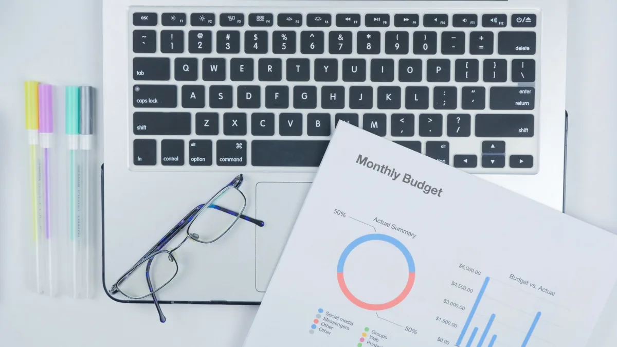 Laptop, lentes y un presupuesto con gráficos sobre un escritorio